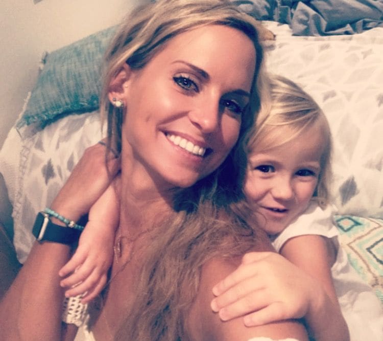Elisabeth smiling on a bed while a little girl hugs her from behind